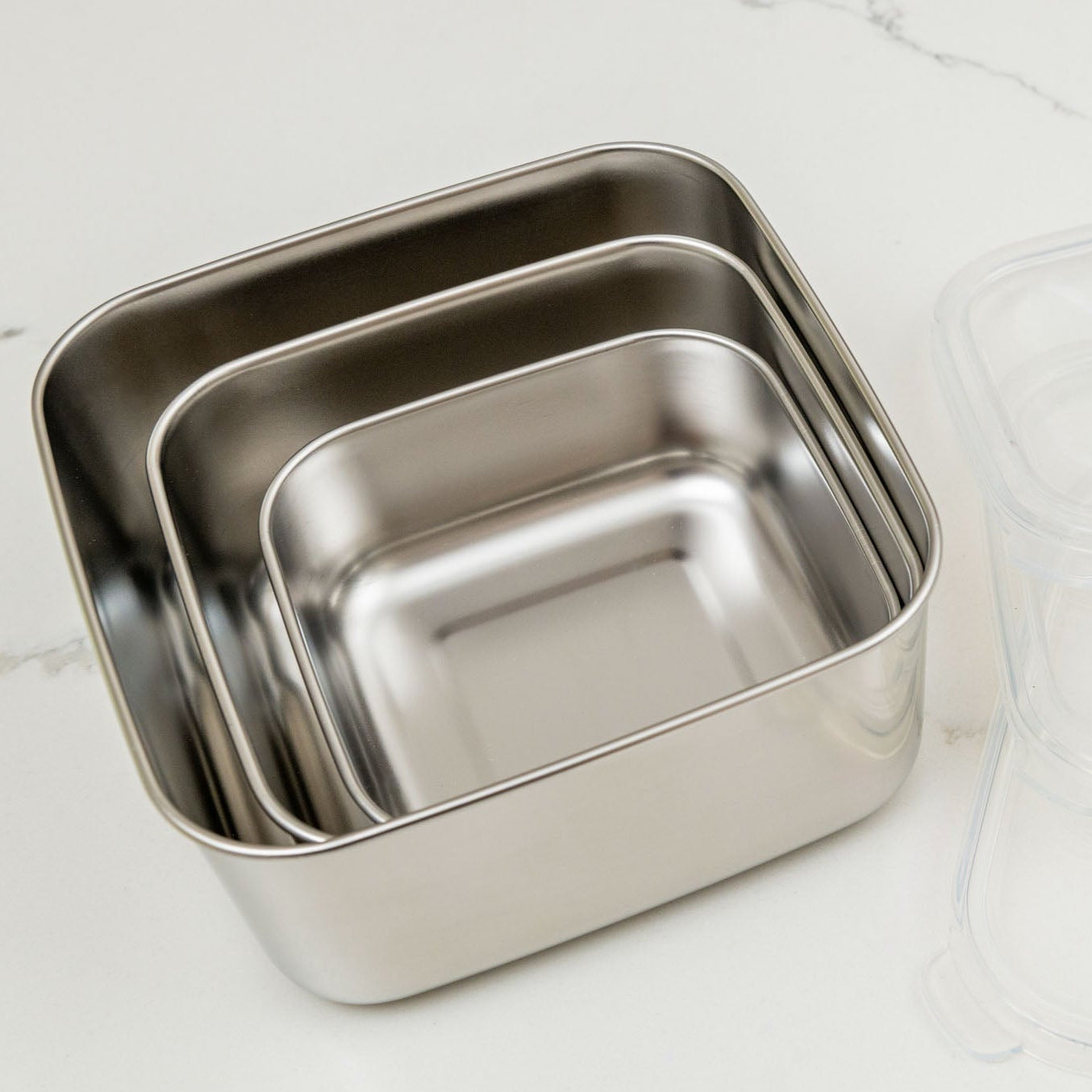 Set of three stainless steel containers with lids on a light gray background